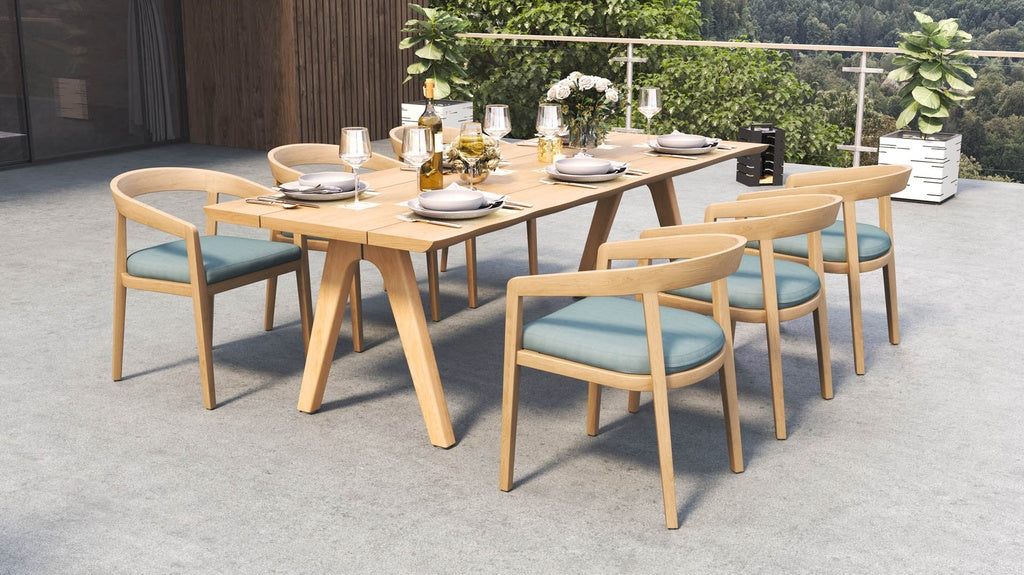 Outdoor dining set on a patio, with a long table and six wooden dining chairs with blue cushions.