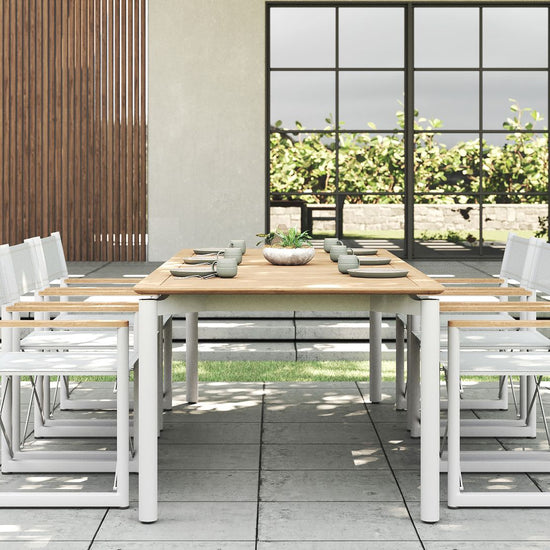 Full outdoor dining set with a premium teak table and six Aleta director chairs with white frames.