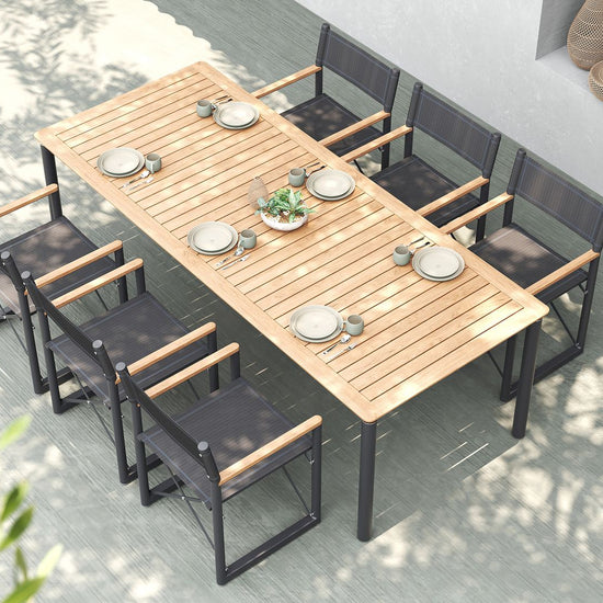 An overhead view of a modern outdoor dining set with long teak table & black Aleta director chairs.