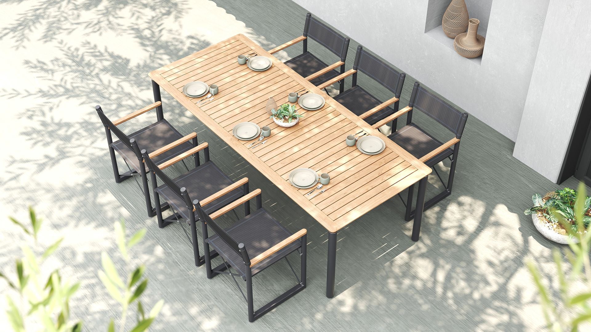 An overhead view of a modern outdoor dining set with long teak table & black Aleta director chairs.