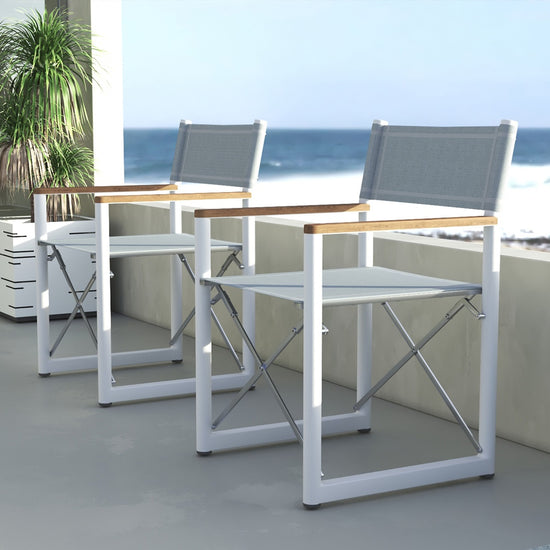 Two white Aleta director chairs with teak armrests on a balcony overlooking the sea by Be A Little.