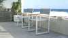 Two white Aleta director chairs with teak armrests on a balcony overlooking the sea by Be A Little.