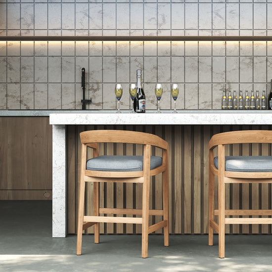 Two wooden counter stools with grey cushions facing a marble-top bar in a modern outdoor kitchen.
