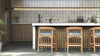 Two wooden counter stools with grey cushions facing a marble-top bar in a modern outdoor kitchen.