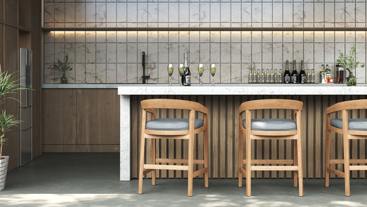 Two wooden counter stools with grey cushions facing a marble-top bar in a modern outdoor kitchen.