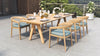 Outdoor dining set on a patio, with a long table and six wooden dining chairs with blue cushions.