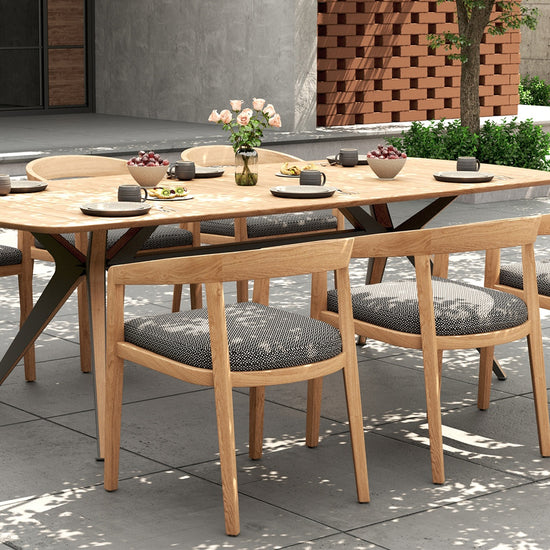 Outdoor dining set with a rectangular wooden table & 6 dining chairs with gray cushions on a patio.
