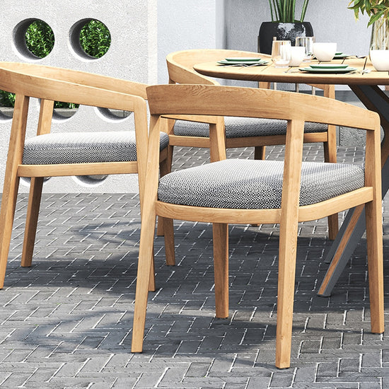 Outdoor dining set on a brick patio, with a round table & outdoor dining chairs with gray cushions.