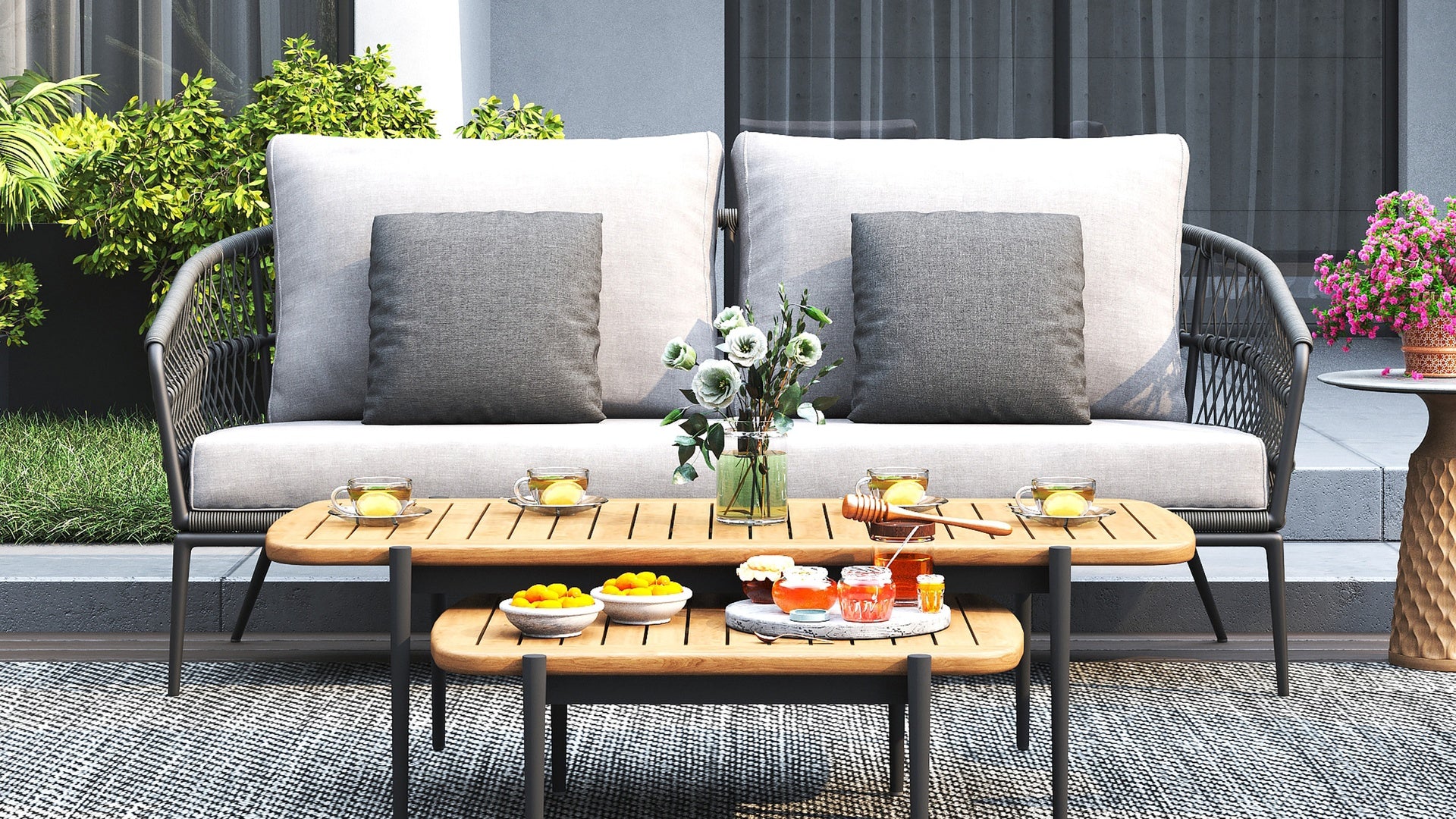 Be a Little's Vino 3-seater sofa styled outdoors with grey cushions, wooden tables, and a tea setup.